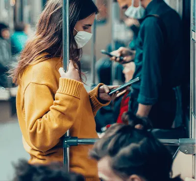 Mulher com uma camiseta laranja utilizando máscara de proteção em transporte público e segurando um celular na mão esquerda